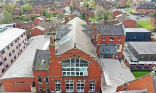Aerial view of a red-brick building amid residential houses and green spaces.